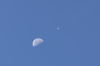 Airbus jet passenger aircraft flying in a blue sky passing by the moon, England, United Kingdom,