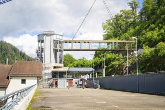 A lifted bridge over a building complex, held by a crane, in sunny weather with blue sky and white