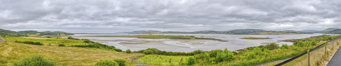 Wide landscape with river and green hills under a cloudy sky, panoramic view, Gweebarray Bay