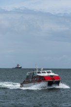 Dune ferry full speed ahead to the offshore island of Helgoland, tugboat on the horizon, North Sea,