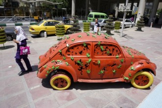 A woman walks past a Volkswagen Beetle art object on the pavement in Tehran. The city of Tehran is