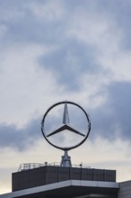 Mercedes star in front of dark clouds, office building at the headquarters of Mercedes-Benz Group