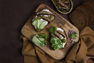 Sandwiches, black bread with sprats, cream cheese, cucumbers, on a cutting board, top view,