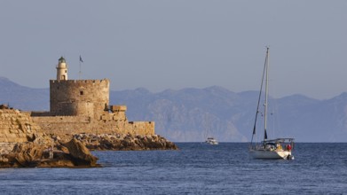 Sailing boat passes old fortress with lighthouse in soft morning light, Fort of Saint Nikolaos,