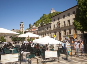 People in tourist cafe in Plaza Nueva, Granada, Spain looking up at part of the Alhambra on a hill