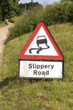 Red triangle road sign warning of Slippery Road, Suffolk, England, Uk