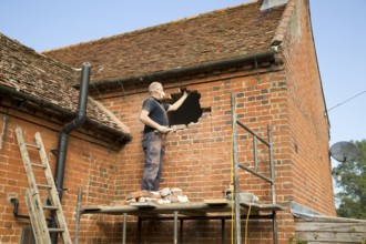 Builder removing red bricks to make window space, Suffolk, England, UK