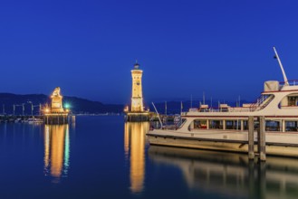 Bavarian Lion, the lighthouse and an excursion boat in the harbour at the blue hour, Lindau Island,