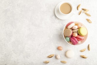 Multicolored macaroons and chocolate eggs in ceramic bowl, cup of coffee on gray concrete