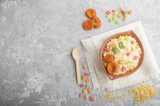 Bulgur porridge with dried apricots and candied fruits in clay bowl on a gray concrete background