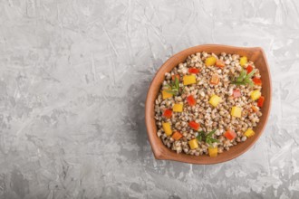 Buckwheat porridge with vegetables in clay bowl on a gray concrete background. Top view, flat lay,