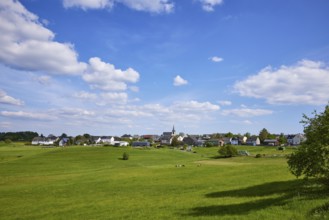 Landscape with meadows under a blue sky with cumulus clouds and a long shot of Kliding, Eifel,