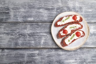 Red beet bread sandwiches with cream cheese and tomatoes on gray wooden background. top view, flat