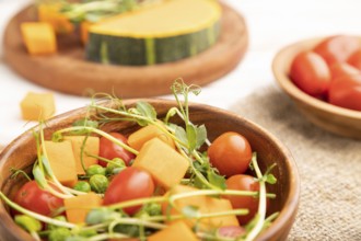 Vegetarian vegetable salad of tomatoes, pumpkin, microgreen pea sprouts on white wooden background