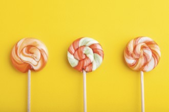 Three lollipop candies on yellow pastel background. copy space, top view, flat lay