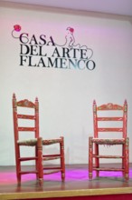 Two decorative red chairs on a stage under the lettering 'Casa Del Arte Flamenco', Granada