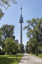 High transmission tower towers above the trees in the municipal park under a blue sky, Vienna