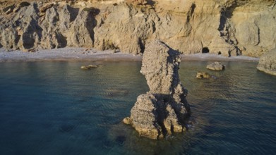 Large, rough rock formation in the calm sea with a coastal backdrop, drone shot, evening light,