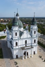 Large baroque church with white facades and green towers in a cityscape in sunny weather, Basilica