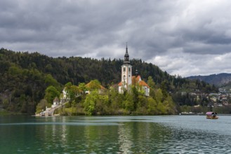 Church on an island in the lake under a cloudy sky, with a boat in the water, Bled Island with St