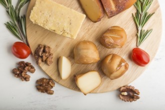 Smoked cheese and various types of cheese with rosemary and tomatoes on wooden board on a white