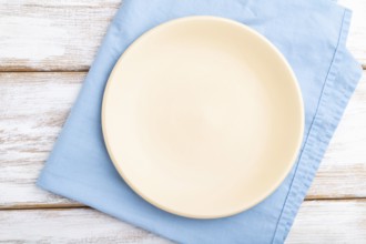 Empty ceramic plate on white wooden background and blue linen textile. Top view, close up, flat lay