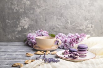 Purple macarons or macaroons cakes with cup of coffee on a gray wooden background and white linen