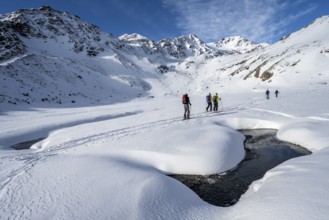 Small stream in a snow-covered mountain landscape, ski tourers in a valley, ascent to the