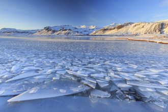 Ice floes on a lake in front of snowy mountains, sun, evening light, snow, winter, Snaefellsnes,