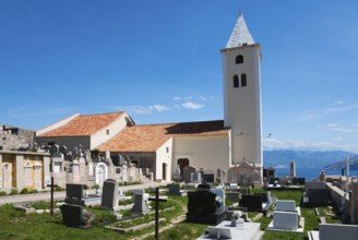 Old church with cemetery and bell tower against a mountain backdrop under a blue sky, Church of St