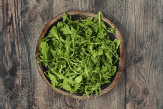 A rustic wooden bowl with fresh arugula leaves on a textured wooden table, showcasing vibrant