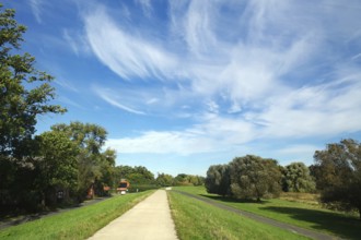 Long path on a dyke under a picturesque sky with clouds and surrounded by green landscape, cycle