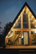 Dreamy woman stands on the doorway of a large wooden cabin late at night