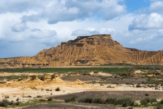 Majestic mountain in a dry desert landscape, partly cloudy with scattered green vegetation against