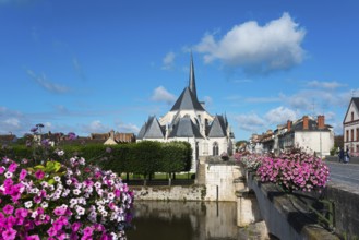 Ansicht einer Kirche in einem kleinen Dorf mit blauen Himmel und weißen Wolken, umgeben von Blumen