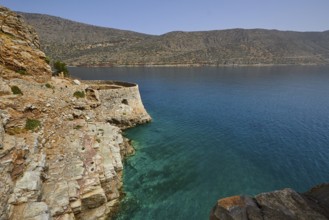 Rustic stone wall on cliffs above a turquoise sea with mountains in the distance, Venetian sea