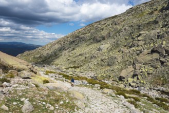 A hiking person on a stony path through a rocky mountain landscape under a cloudy sky, Hiking area,