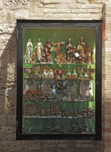 Shop window with figures of saints, devotional objects, in the historic centre of Assisi, Umbria,