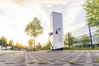 An electric charging station on a cobblestone street at sunset, surrounded by trees and urban