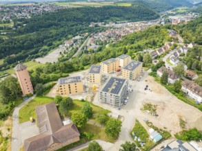 View of a construction site and surrounding residential buildings with roofs in a green landscape,