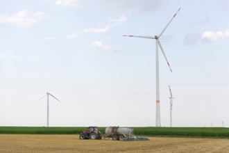 Farmer spreading liquid manure on a harvested grain field, wind farm, defective wind turbine with a