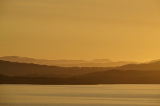 Calm atmosphere over the sea, hills and an orange sunrise, autumn, Bergen, North Sea, Norway,