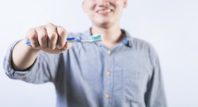 Smiling person showing toothbrush with toothpaste isolated. Unrecognizable man holding brush with