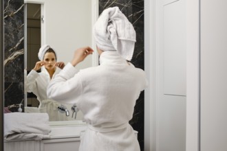 Woman wrapped her hair in towel after shower looking in mirror and fixing towel