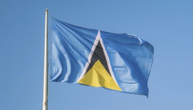 The flag of St Lucia, Caribbean, flutters in the wind, isolated against a blue sky