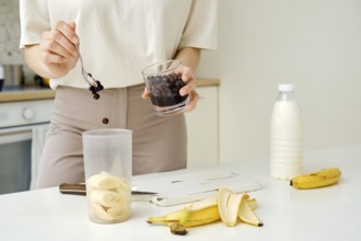 Unrecognizable woman puts blackcurrants in a blender to mix them with a chopped banana