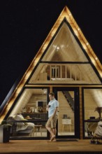 Man with a glass in his hand standing on terrace of tiny house at late evening and enjoys calmness