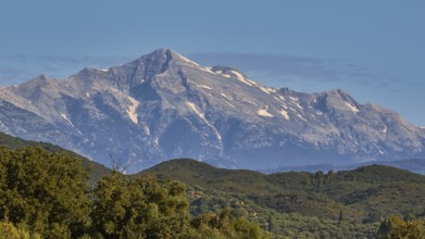 A majestic, snow-capped mountain peak rises above green forests, Taygetos Mountains, Mani