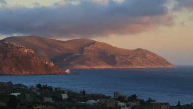 A mountain landscape at dusk with a view of the sea and a small settlement in the foreground, Mani