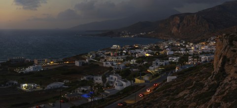 Illuminated town of Arkasa at dusk with surrounding mountains and sea in the background, Arkasa,